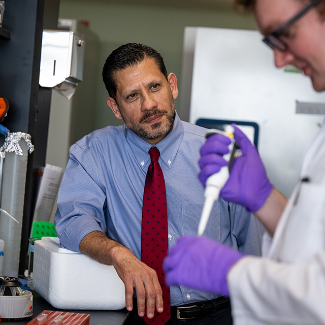 Felipe Andrade in a lab setting with a colleague wearing a light blue button down shirt and red tie