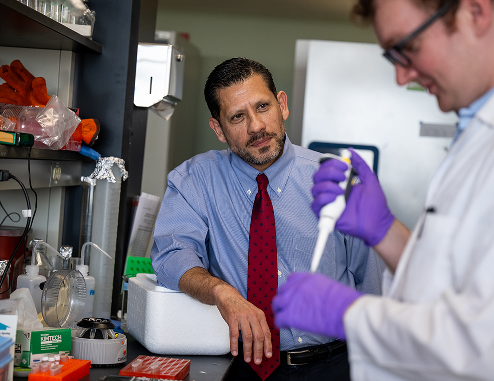 Felipe Andrade in a lab setting with a colleague wearing a light blue button down shirt and red tie