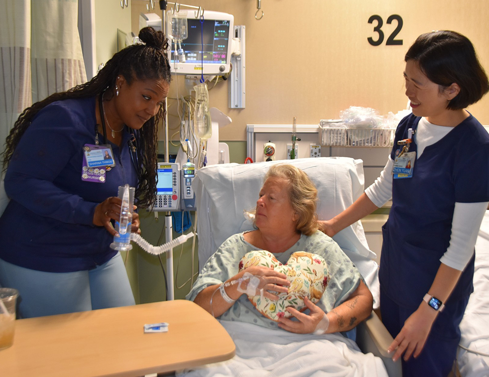 Patient Fran holds a heart-shaped pillow given to her by students and nurse Zhen Yuan