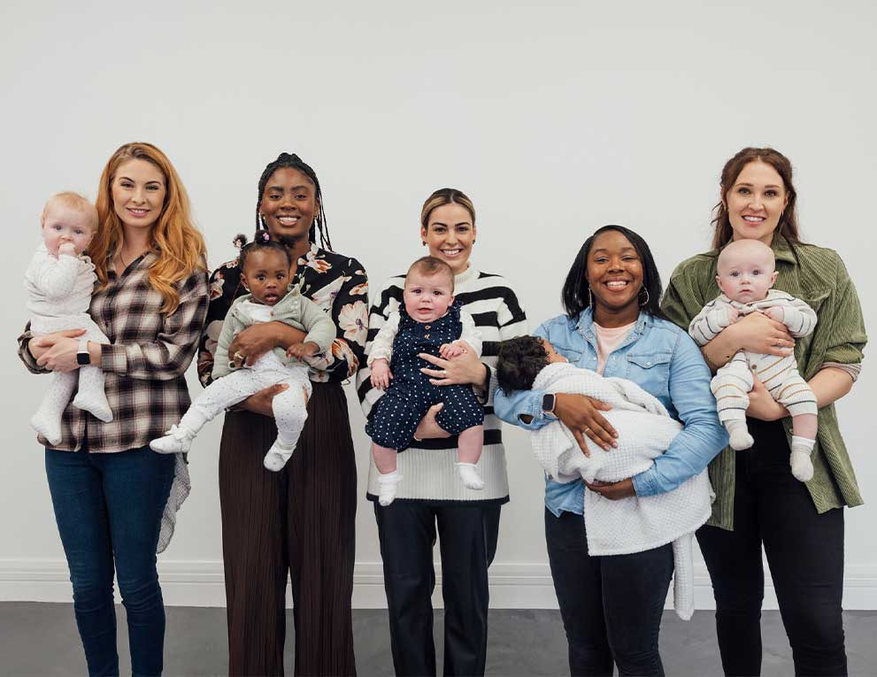 Five moms standing in a line holding their babies