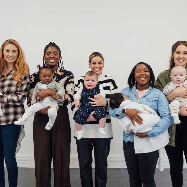 Five moms standing in a line holding their babies