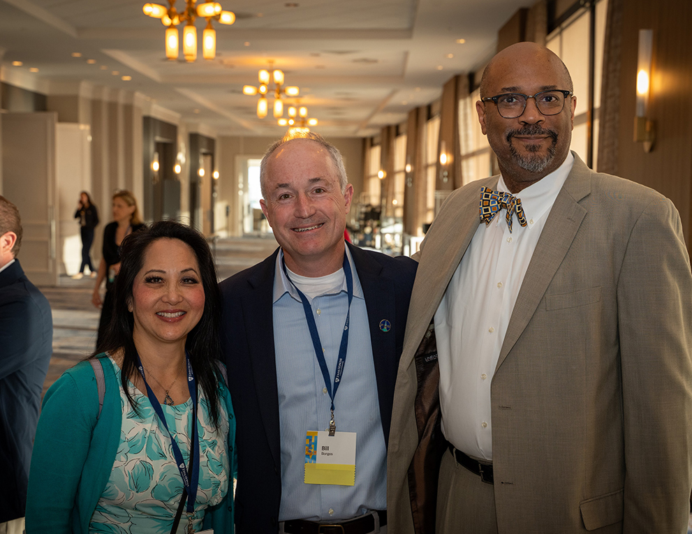 Three alumni stand, smiling for a picture.