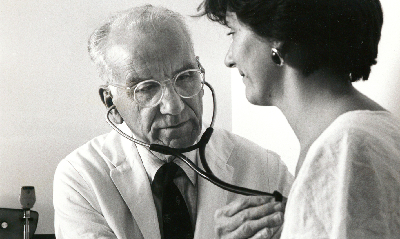 An elderly VICTOR MCKUSICK listens to the heart of a female patient.