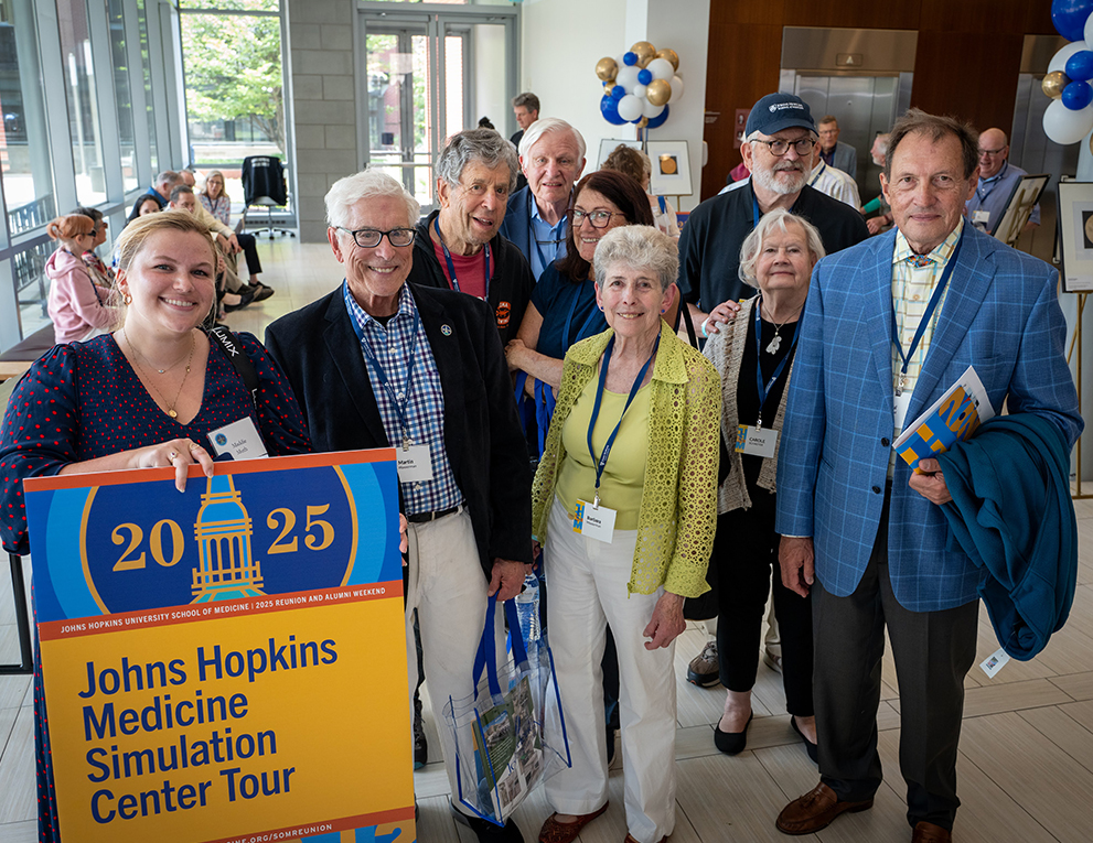A group of alumni stand together with a sign