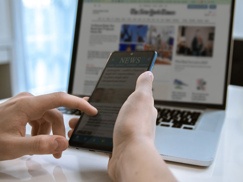 Hand browsing news on cellphone and laptop