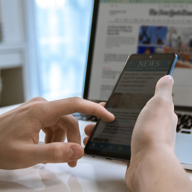 Hand browsing news on cellphone and laptop