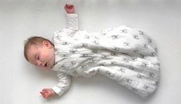 Infant laying on it's back with it's arms wide, sleeping peacefully. 