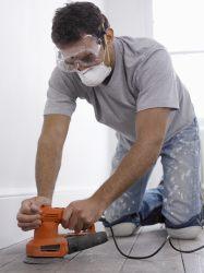 Man wearing a face mask while sanding a wood floor.