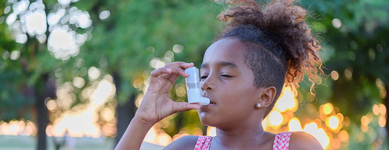 A young girl uses an inhaler while outdoors