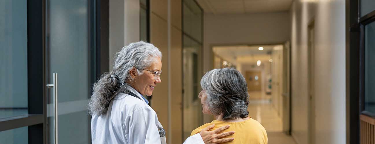 Woman speaks with her doctor as they walk through a hallway together