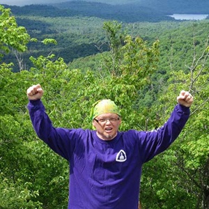 Craigs throws his hands in the air in celebration at the summit of a hiking trail.