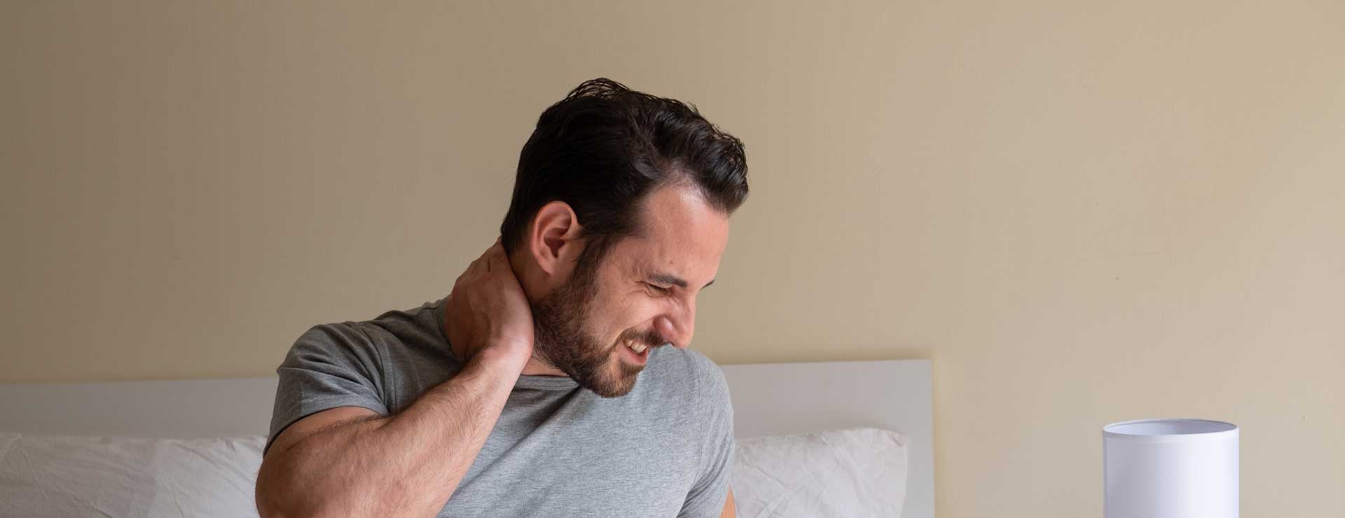 Man holding his neck in pain in his bedroom.