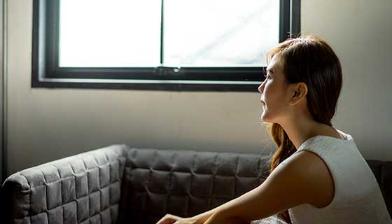 A woman sits alone, looking out a window.