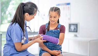 Health care provider examining girl's arm in cast.