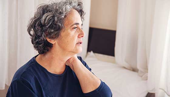 A woman rubs her neck in pain while looking out the window.
