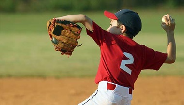A young boy winds up his arm to pitch a baseball.