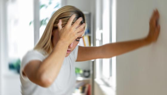Woman with headache leaning against wall