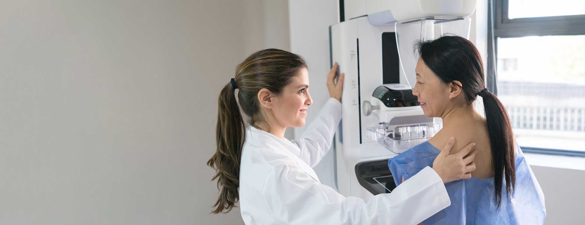 A doctor helps a patient get into position for a mammogram.