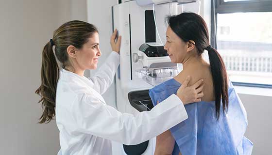 A doctor helps a patient get into position for a mammogram.
