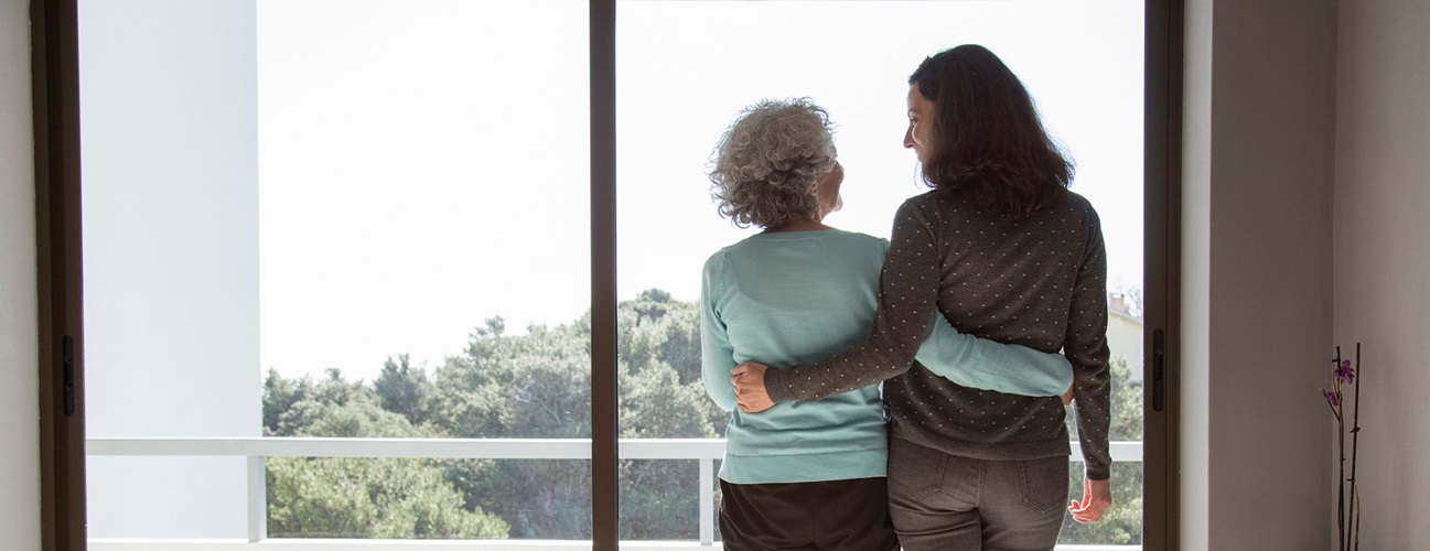 a mother and her adult daughter have their arms around each other as they look out a window