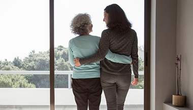 a mother and her adult daughter have their arms around each other as they look out a window