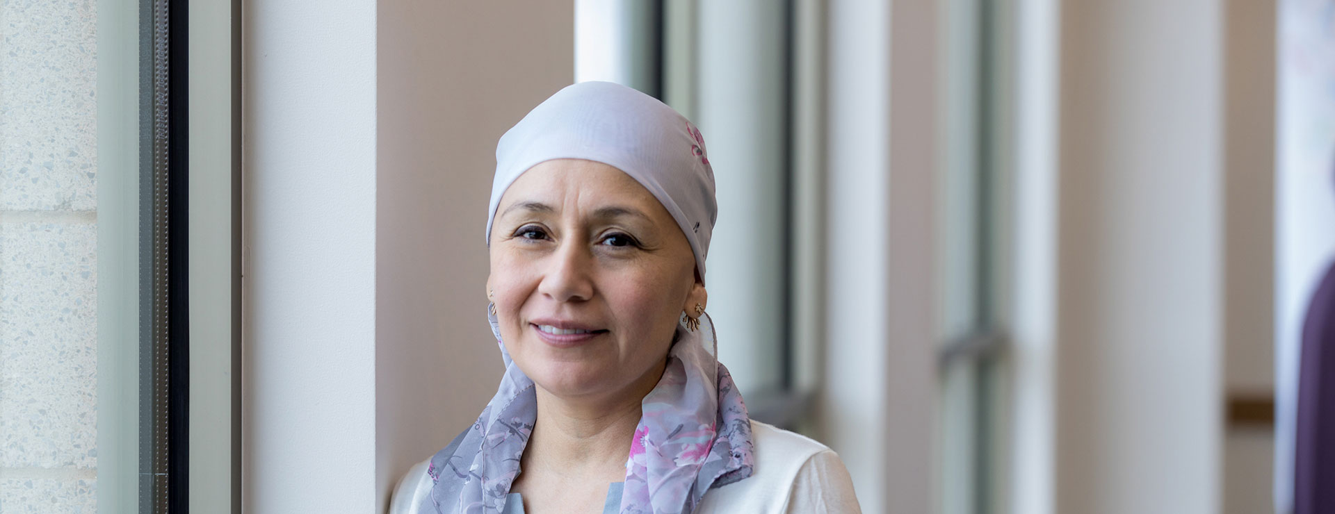 a woman wearing a headscarf poses by a window