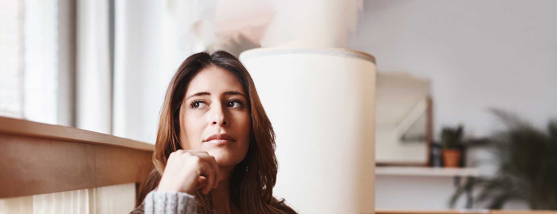 A woman sits in front of the window, looking thoughtful.