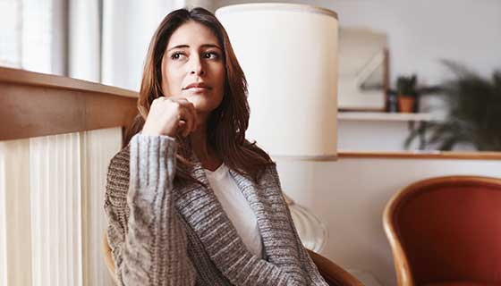 A woman sits in front of the window, looking thoughtful.