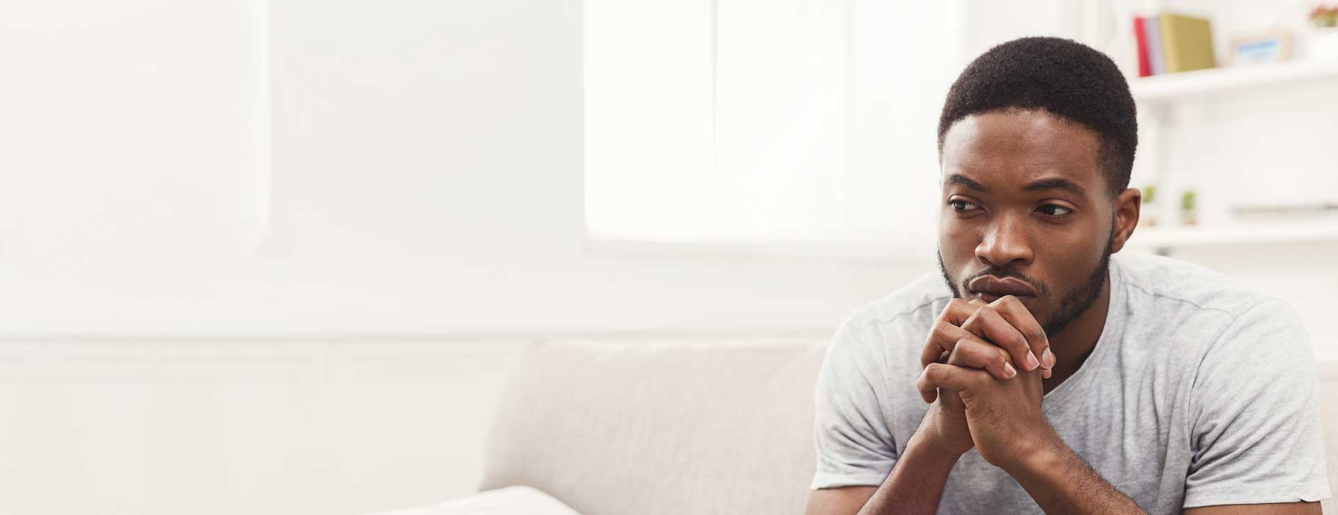 A young man sits pensively on the couch.