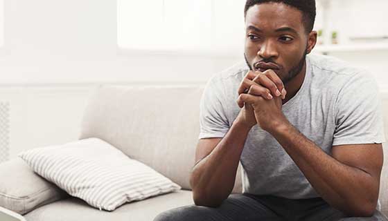 A young man sits pensively on the couch.