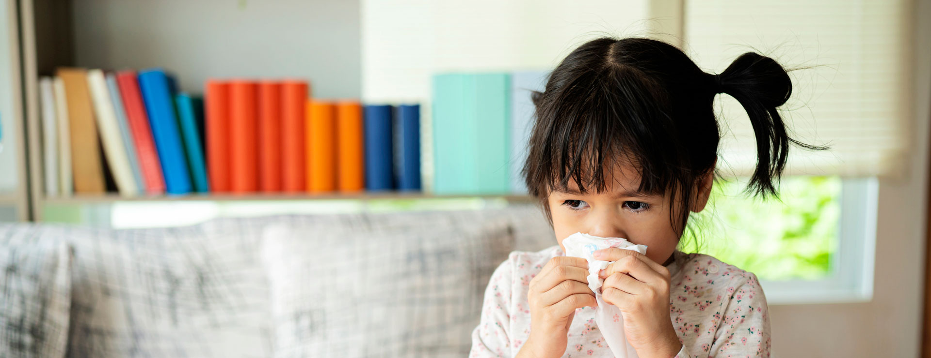 A little girl wipes her nose with a tissue.