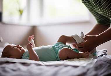 a mother changes the diaper of a baby with necrotizing enterocolitis