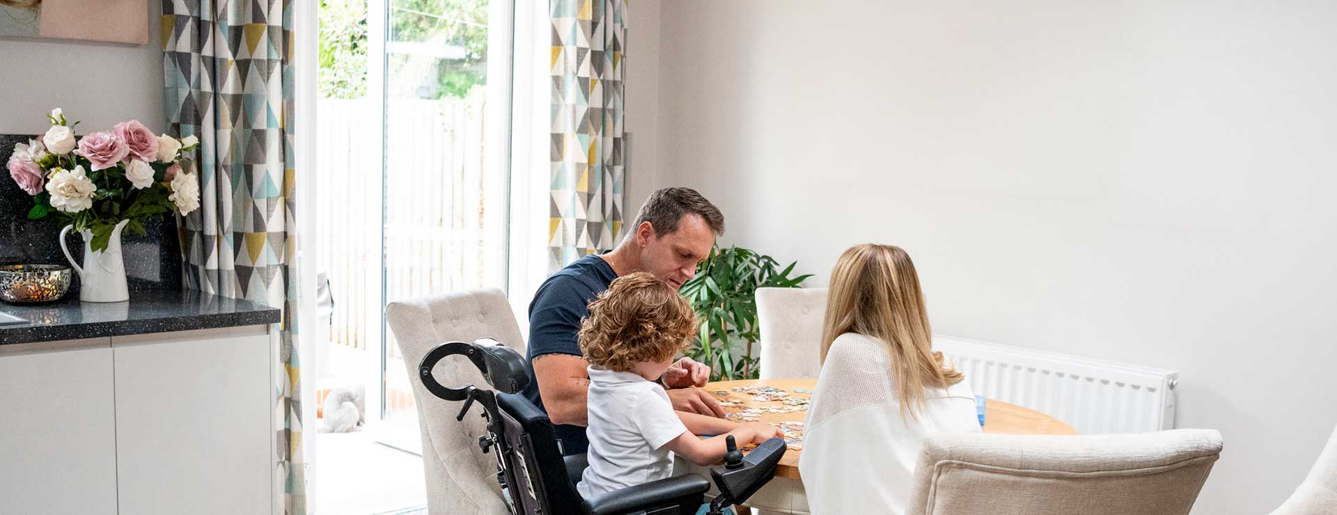 Child with muscular dystrophy with parent's doing a puzzle at table