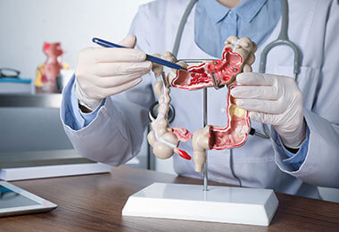 a doctor uses a pen to gesture to parts of the colon as they describe colon cancer symptoms