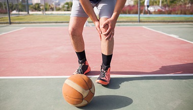 a basketball player clutches his knee in pain