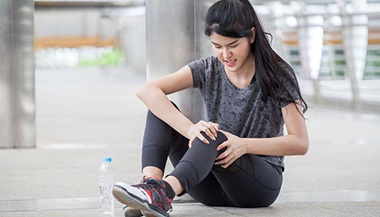 a runner sits on the ground and clutches her knee