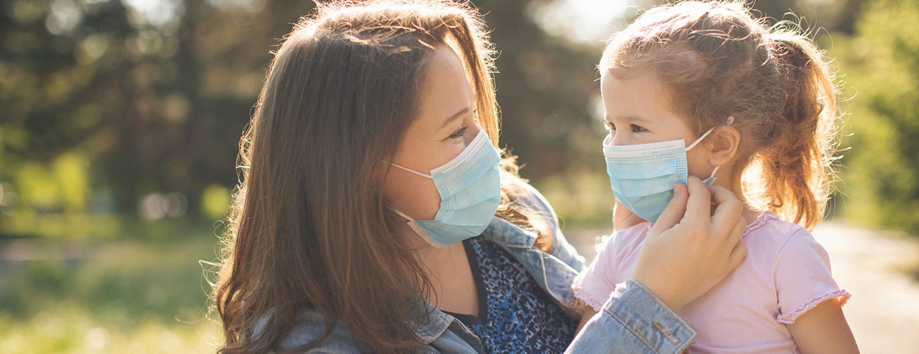 covid family safety - woman helping young daughter put on mask.