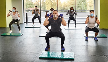 masked gym-goers participate in a group exercise class