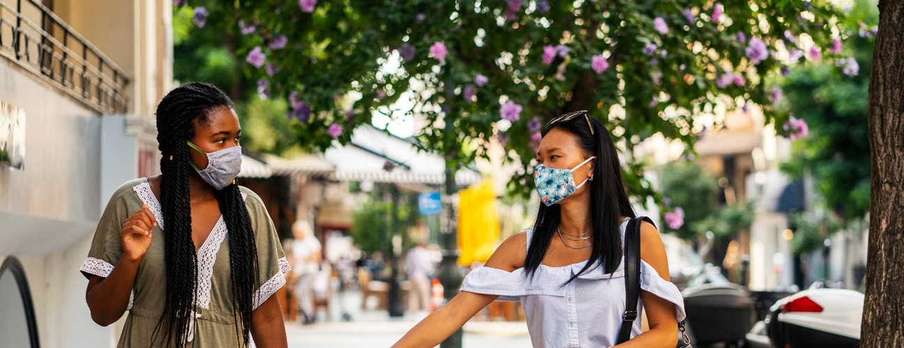 Two women walk down the street together wearing masks