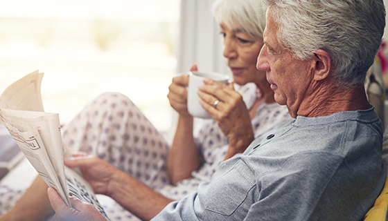 Older couple sitting on the couch together and reading a newspaper