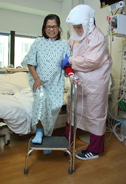 A patient undergoes physical therapy with specialists wearing PPE.
