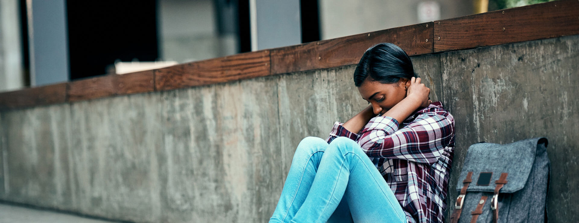 Teenage girl sitting with head down on the sidewalk with a backpack