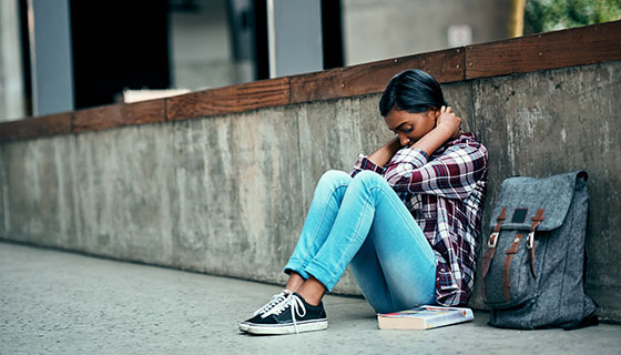 Teenage girl sitting with head down on the sidewalk with a backpack