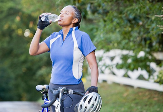Woman on a bike takes a sip of her water bottle while biking through a wooded area.