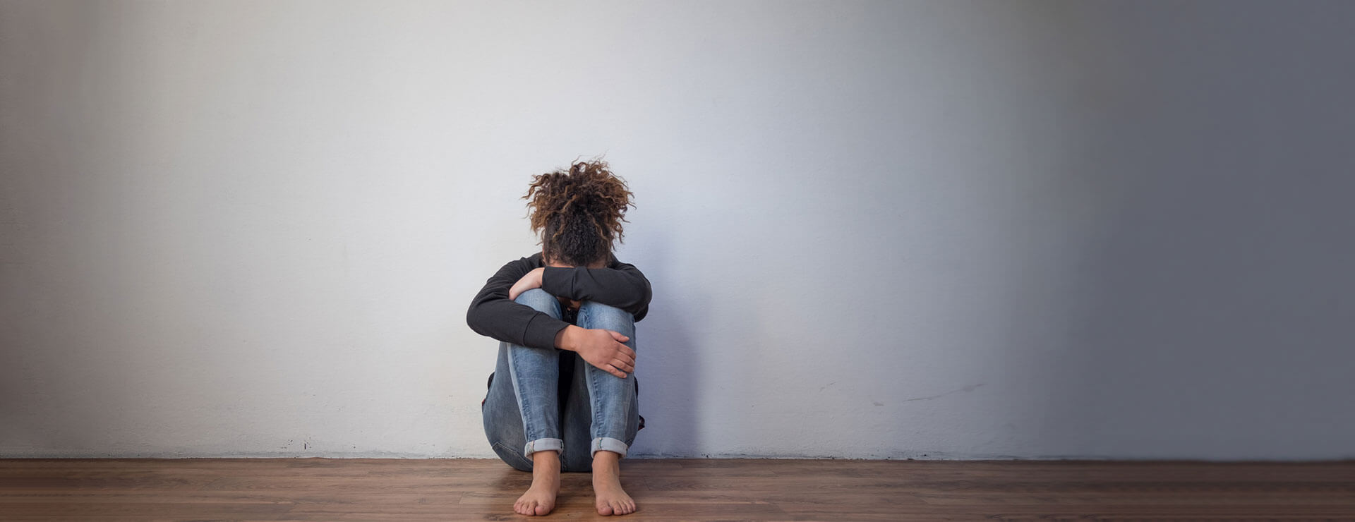 teen sits against wall with head against their knees