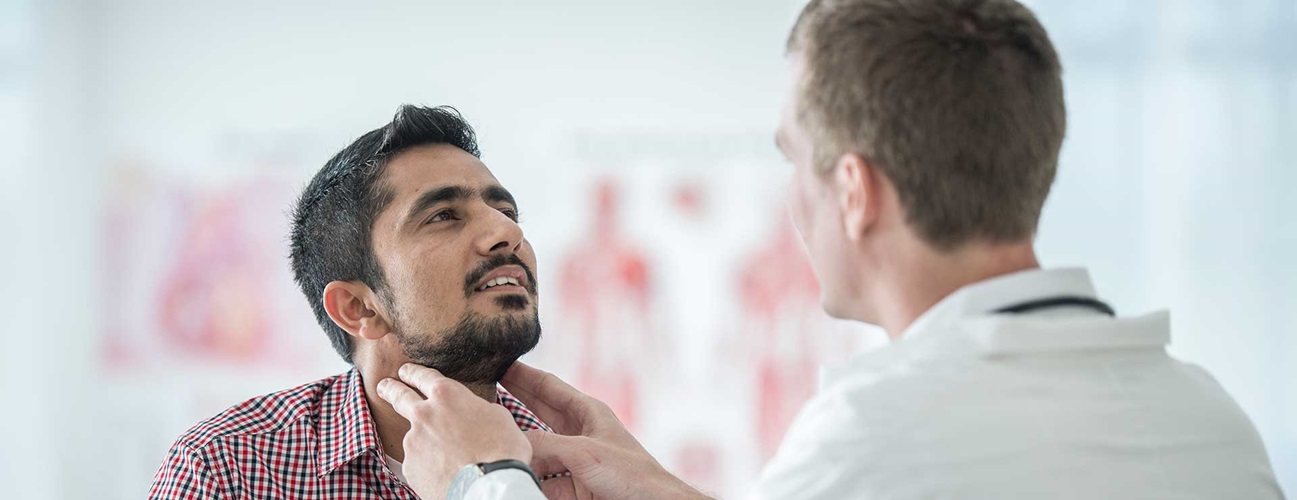 a doctor feels the neck area of male patient to check thyroid