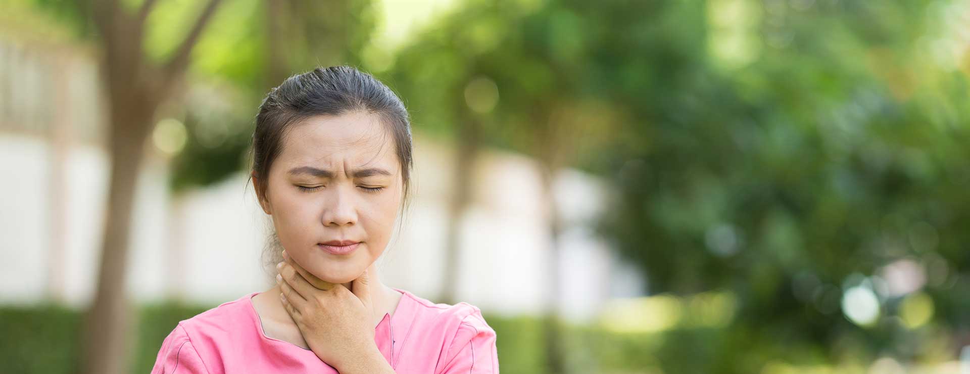 A woman rubs her throat in discomfort.
