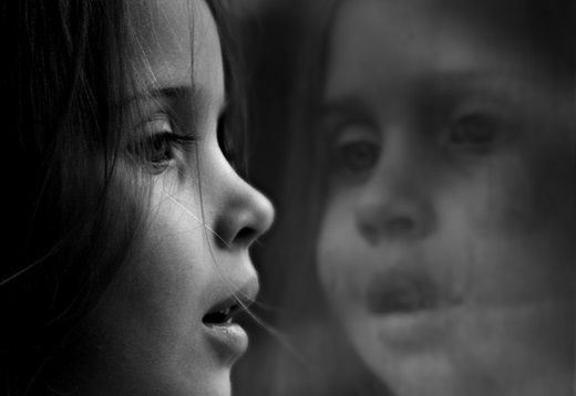 Black and white photo of little girl staring out a window