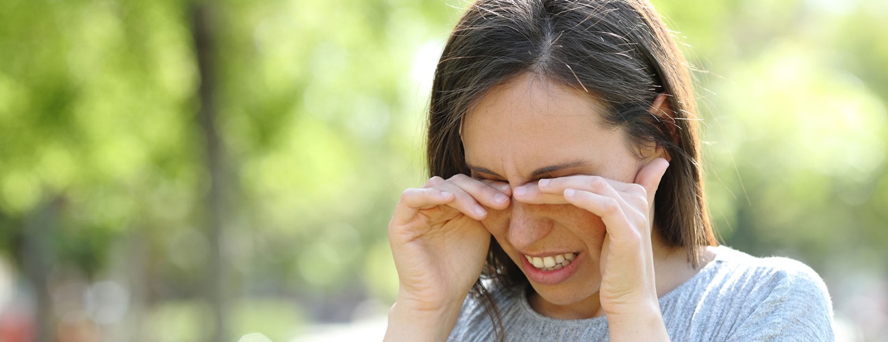 A woman rubs her eyes while outdoors