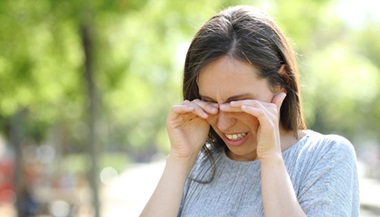 A woman rubs her eyes while outdoors.